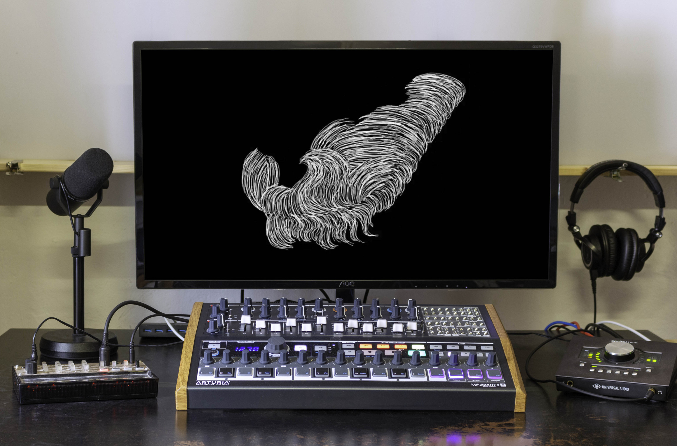 Schreibtisch mit Bildschirm, Kopfhörern, Mikrofon und Mischpult. Auf dem Bildschirm ist ein Standbild des Musikvideos zu sehen: eine abstrakte weiße Form auf schwarzem Hintergrund.