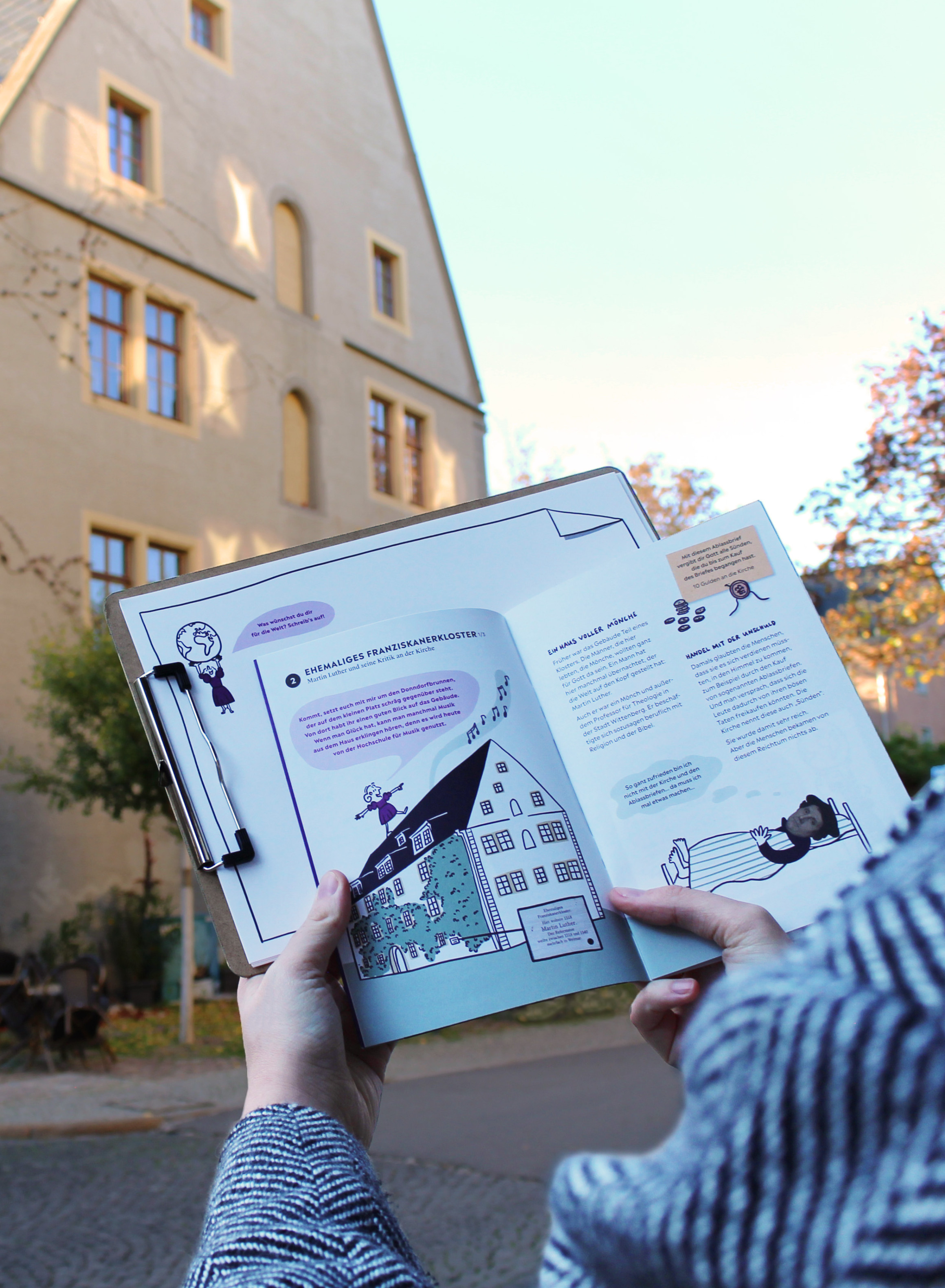 Jemand hält das Heft und ein Klemmbrett vor dem ehemaligen Franziskanerkloster.