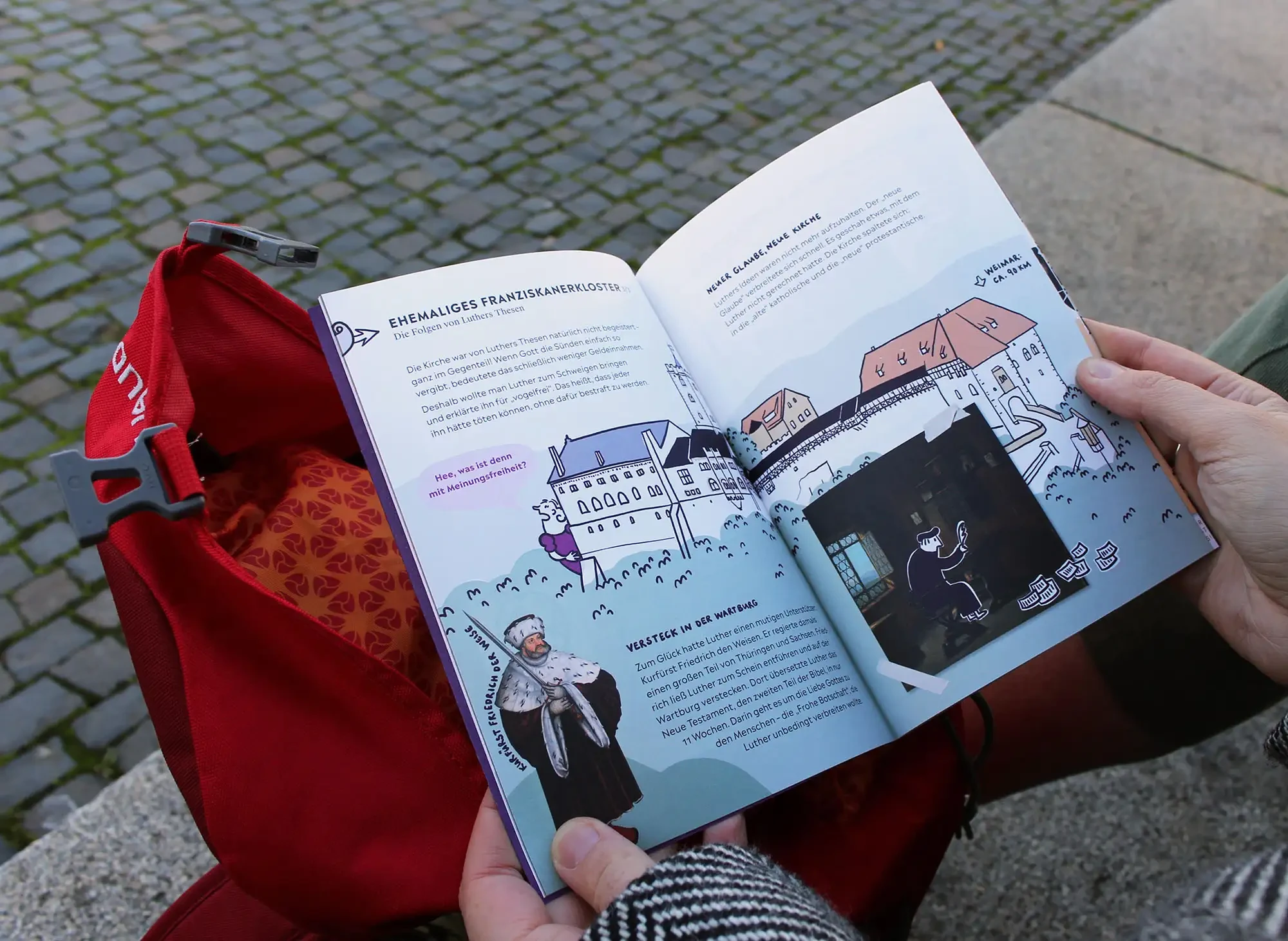 Das aufgeschlagene Heft und der rote Entdeckerrucksack.