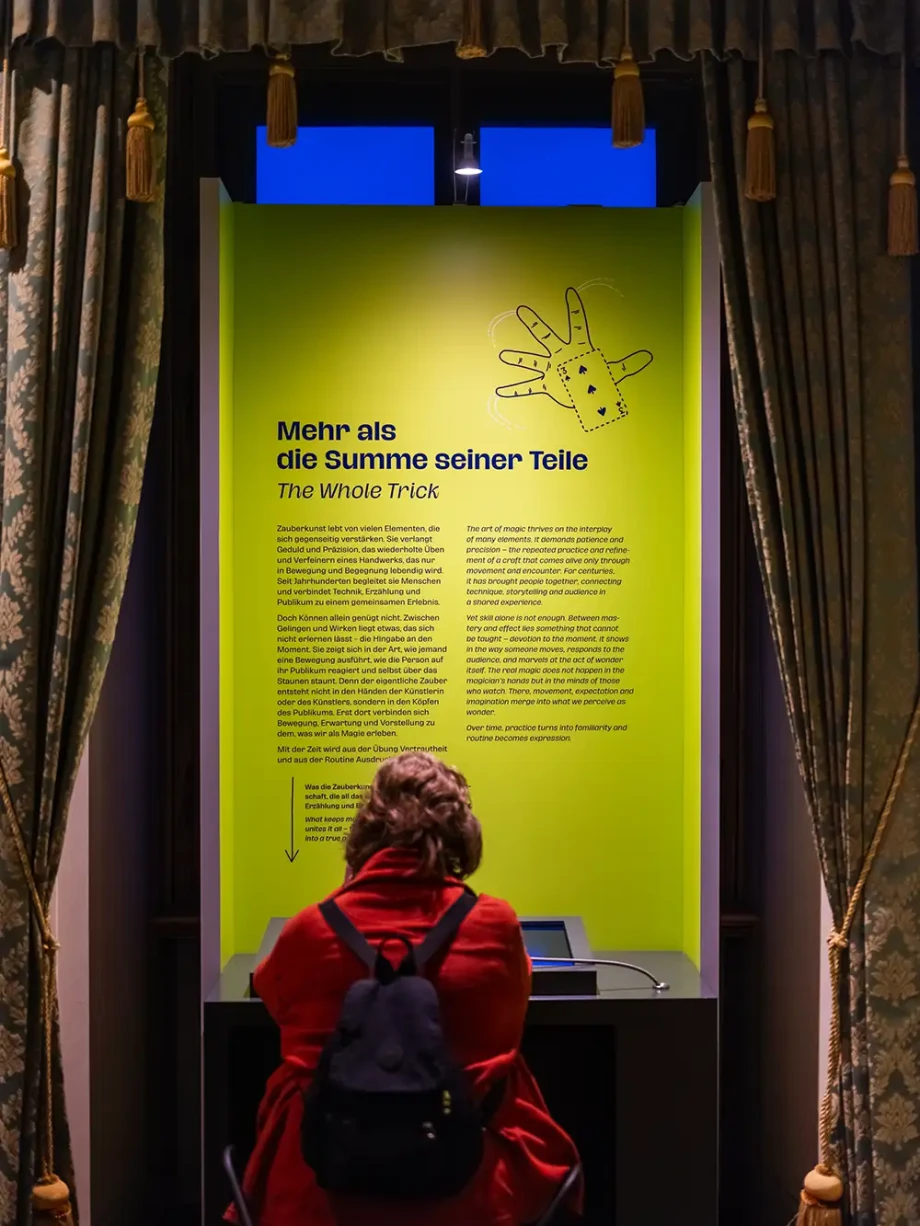 Detail im dritten Ausstellungsraum. Eine Person sitzt vor einer Texttafel an einer Medienstation.